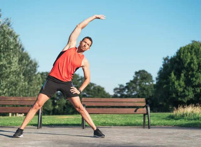 Man performing a side stretch in a park, illustrating the importance of balance and stability exercises with Fitknit grip socks