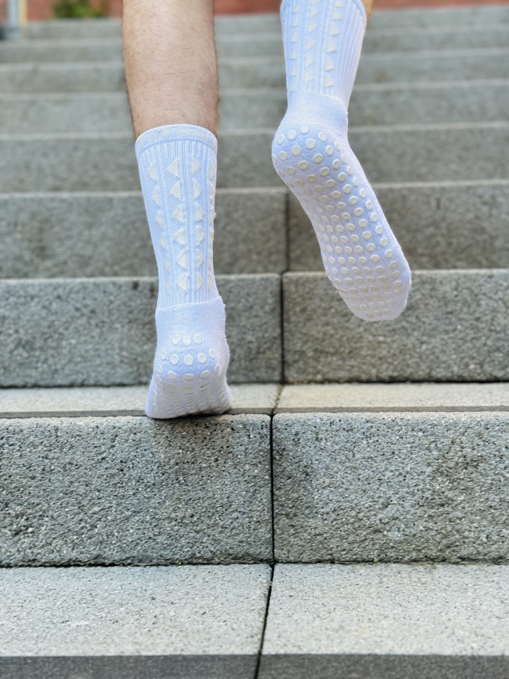 FitKnitSocks white grip socks with anti-slip soles and geometric pattern, worn by a person walking up concrete stairs.